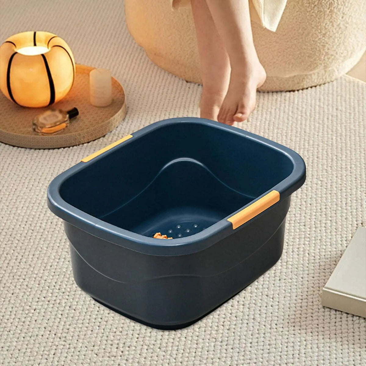 Bain de pied - Bassin portable pour un bain relaxant des pieds – bassin en plastique bleu avec poignées orange, placé sur un tapis près d'une bougie.