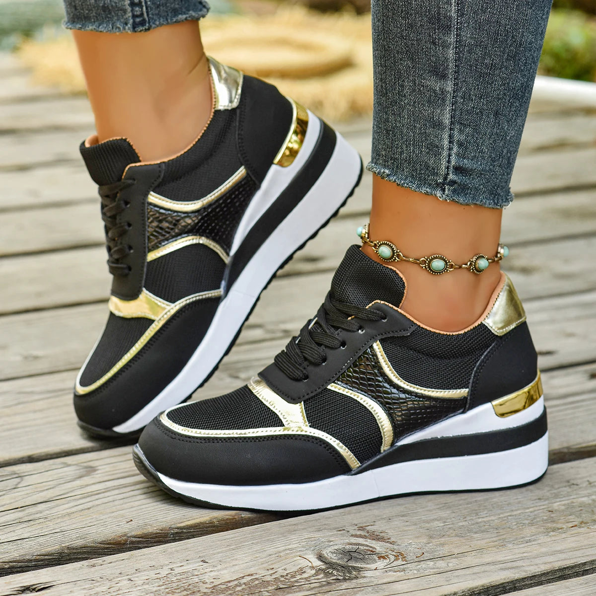 Basket orthopédique femme - Sneakers légères à lacets noires avec détails dorés, portées sur une surface en bois