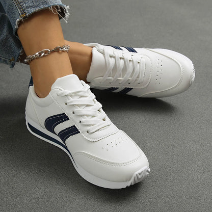 Basket orthopédique femme blanches avec rayures navy, légères et respirantes, portées avec un jean, vue de près sur le pied.
