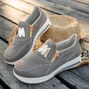 Basket orthopédique femme - Sneakers grises avec logo sur le dessus et semelle blanche, posées sur une surface en bois