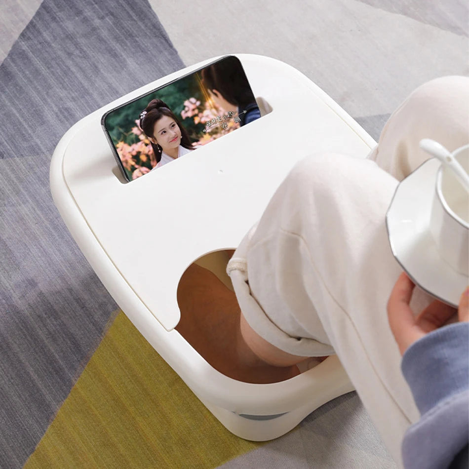 Bain de pied - Bassin pliable ergonomique pour usage à domicile et en – bassin blanc avec une personne assise, les pieds dans l'eau, tenant une tasse.