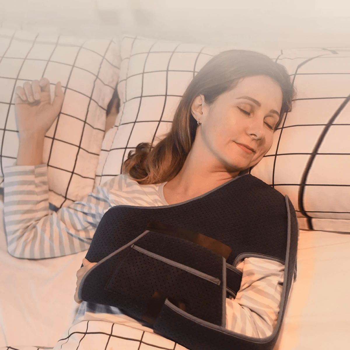 Attelle bras épaule noire en tissu mesh, portée par une femme allongée sur le côté, montrant son confort et son ajustement sur le corps.