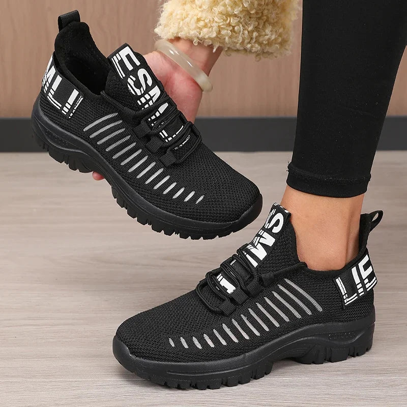 Basket orthopédique femme - Chaussures légères noires avec lanières blanches, vue de côté portée par une femme en leggings.