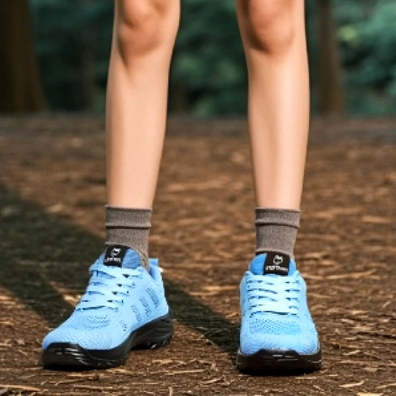 Basket orthopédique femme - Chaussures de sport respirantes en maille bleu clair avec semelle noire, portées sur un sol en terre battue.