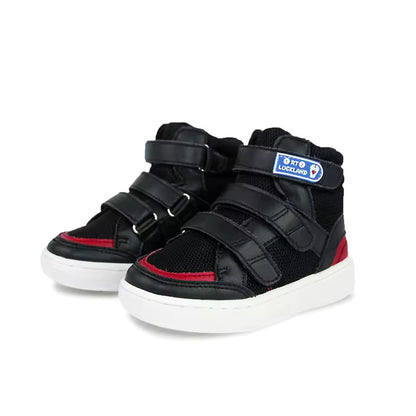 Chaussures orthopédiques enfant FlexiFit – Baskets noires avec détails rouges et fermetures velcro, vue de face sur fond blanc.
