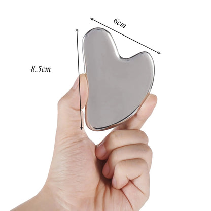 Appareil massage visage en acier inoxydable – forme unique en cœur, tenu dans une main, montrant sa finition brillante et ses dimensions
