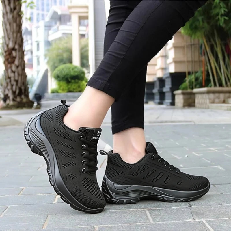 Basket orthopédique femme - Chaussures de sport respirantes en maille noire avec semelle amortissante, portées sur un chemin urbain.