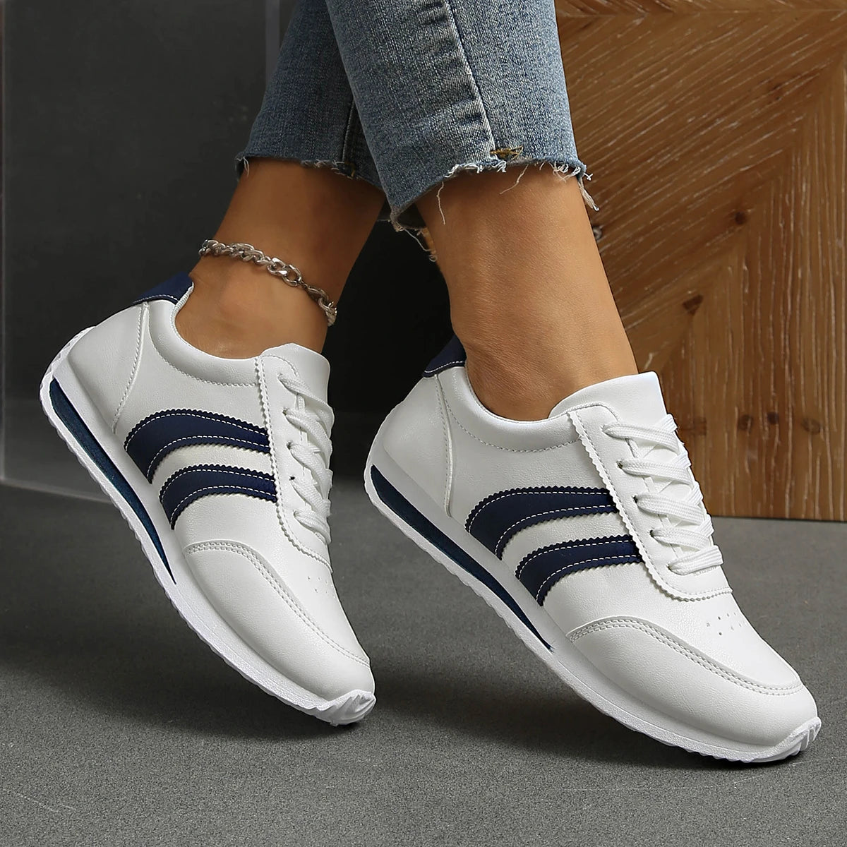 Basket orthopédique femme blanches avec rayures navy, légères et respirantes, portées avec un jean, vue de côté sur le pied.