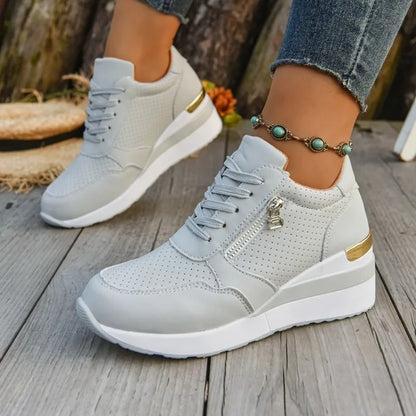 Basket orthopédique femme - Sneakers légères grises à semelle épaisse, avec zip et détails dorés, portées sur un sol en bois.