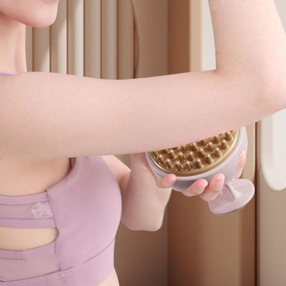 Brosse de massage anti-cellulite manuelle en silicone rose avec picots dorés, utilisée sur le bras d'une personne, vue rapprochée.