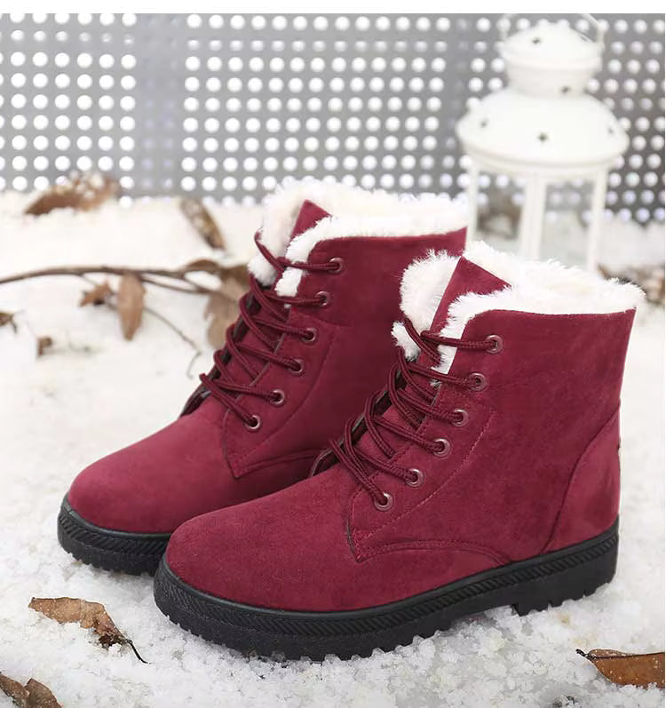 Bottines à Lacets Femme en suède bordeaux avec doublure en fourrure, posées sur la neige, avec des feuilles sèches en arrière-plan.