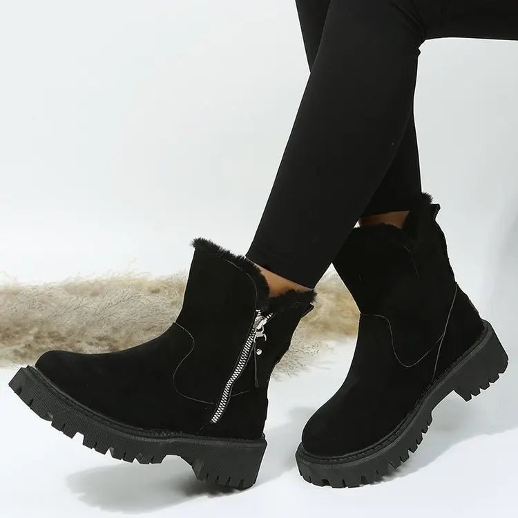 Bottes de Neige Femme noires, fourrées et chauffantes, avec zip latéral, portées avec un pantalon noir, sur fond clair.