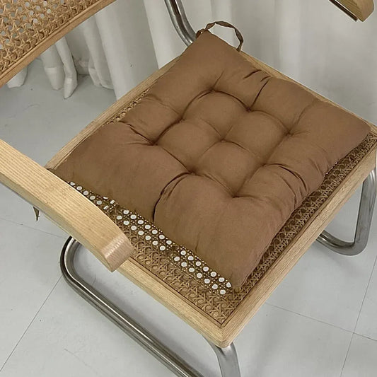 Coussin Orthopédique pour Position Assise – coussin marron sur une chaise en bois avec texture rembourrée et coutures visibles